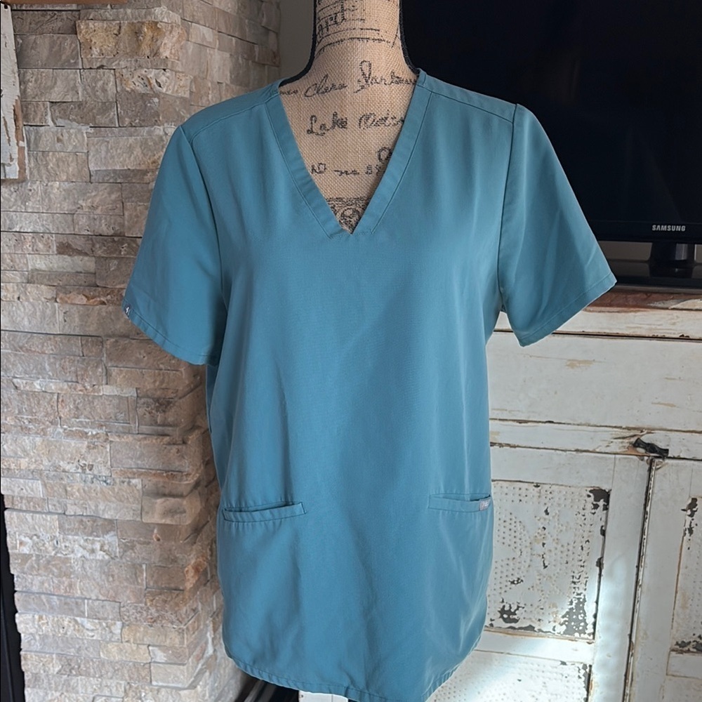 FIGS v-neck short sleeve two front pocket scrub shirt in a blue green color